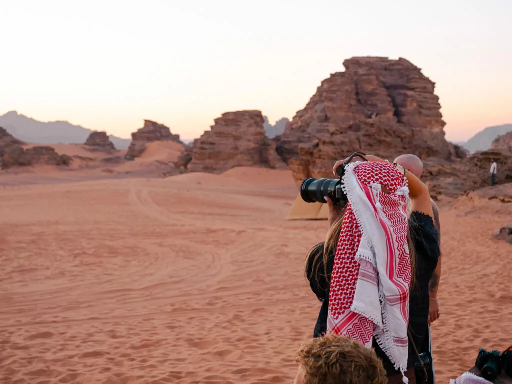Photographer in a red and white keffiyeh photographing the desert landscape in Wadi Rum, Jordan