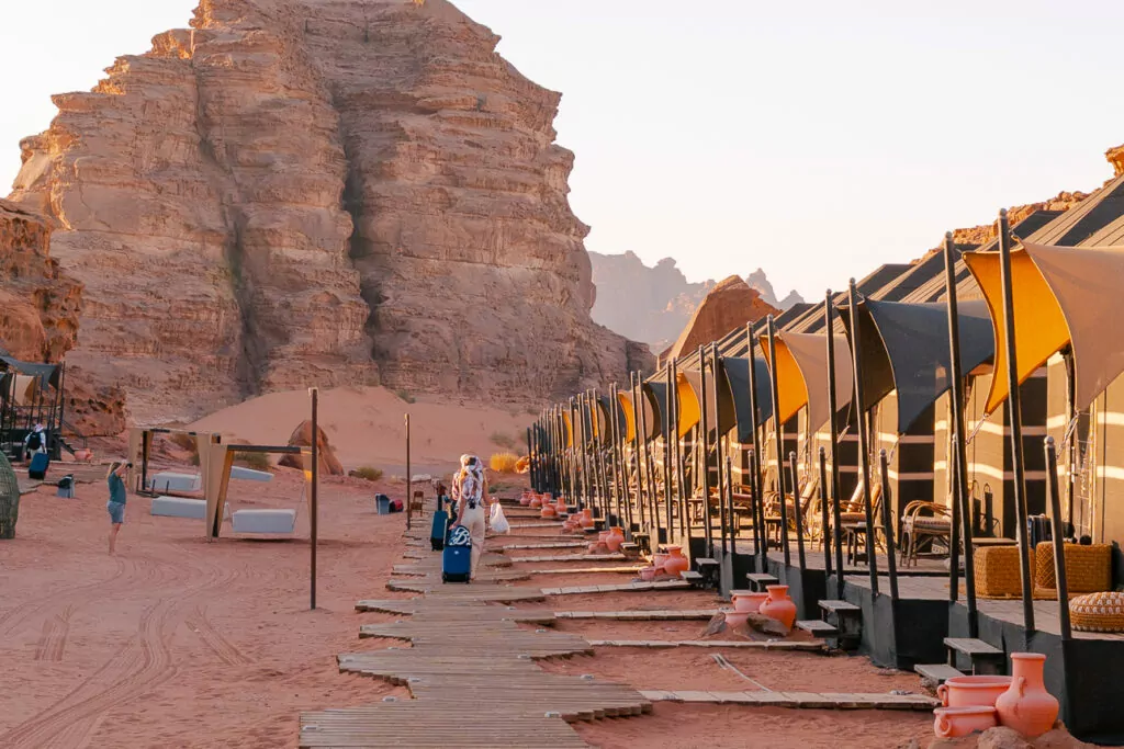Bedouin desert camp in Wadi Rum with colourful open-air tents nestled against towering red sandstone cliffs, visited on a G Adventures Jordan tour