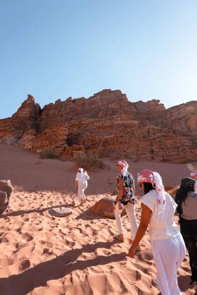 G Adventures tourmates in traditional Bedouin headscarves walking across the red sand in Wadi Rum, Jordan
