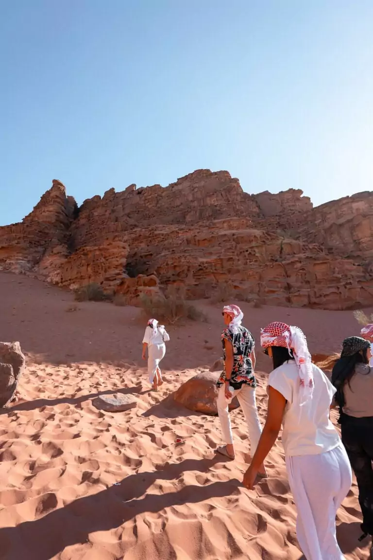 G Adventures tourmates in traditional Bedouin headscarves walking across the red sand in Wadi Rum, Jordan