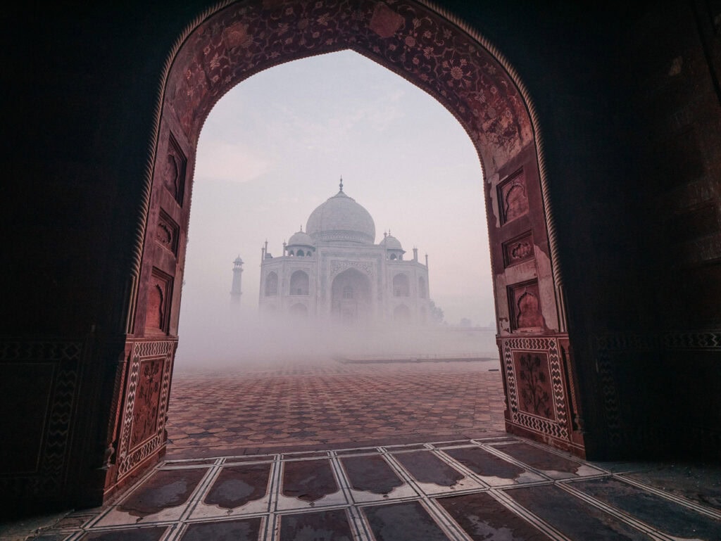 Taj Mahal seen through a large red sandstone archway in thick morning fog