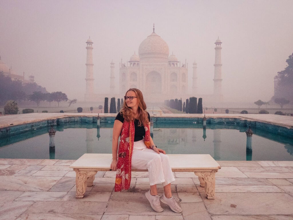 Alexx sitting on the Princess Diana bench in front of the Taj Mahal on a foggy morning, a classic moment from a solo trip in India