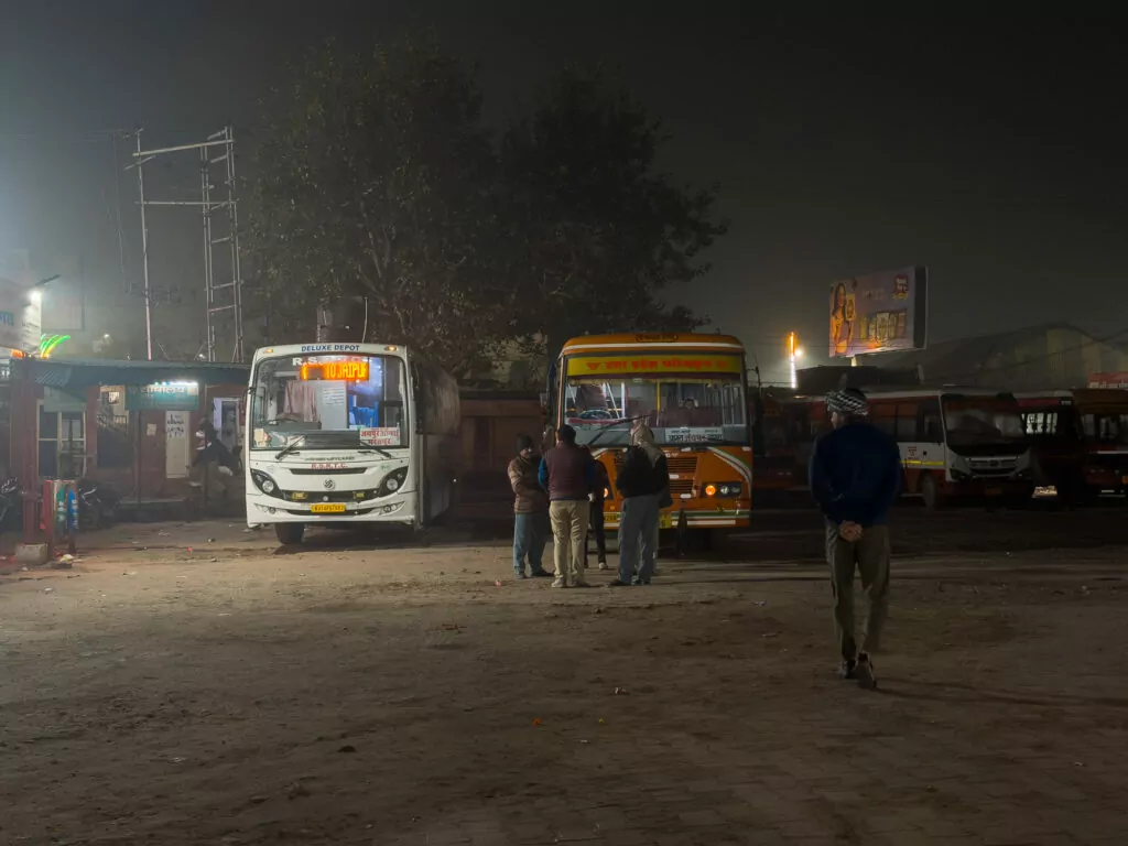 Early morning bus stop with a coach parked in low light and a few people waiting nearby, reflecting the experience of travelling India solo