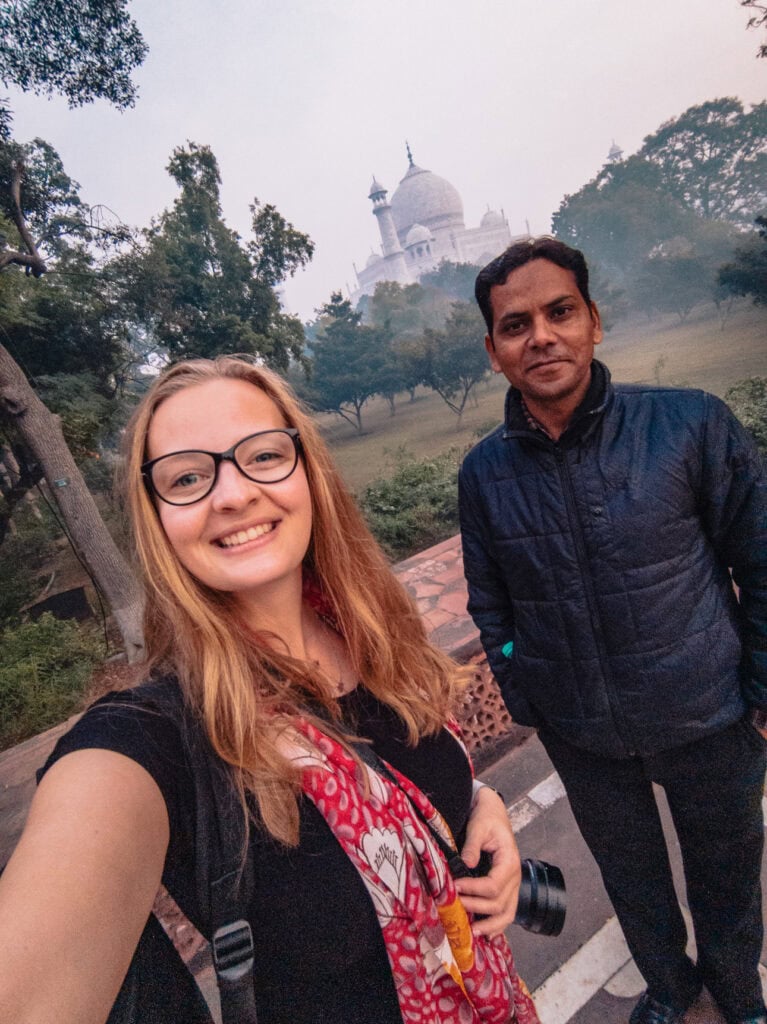 Alexx smiling with her guide in front of the Taj Mahal in soft morning light