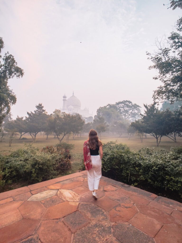 Taj Mahal viewed across gardens on a misty morning with soft light and visitors walking along the path