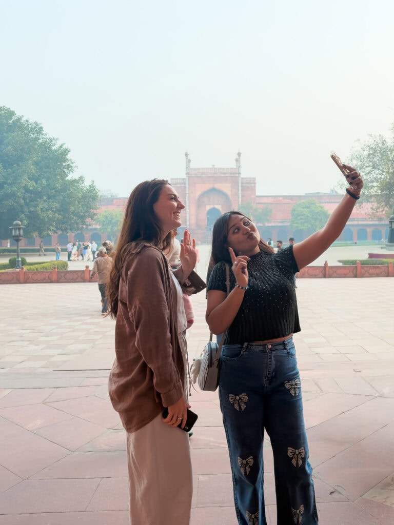 Local woman taking a selfie with a female traveller in front of a historic monument at the Taj Mahal