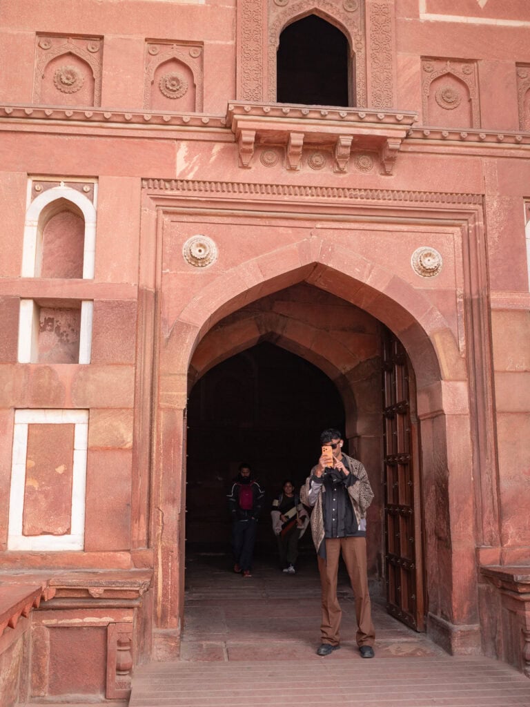 Local man photographing a group of tourists near a large red sandstone gateway