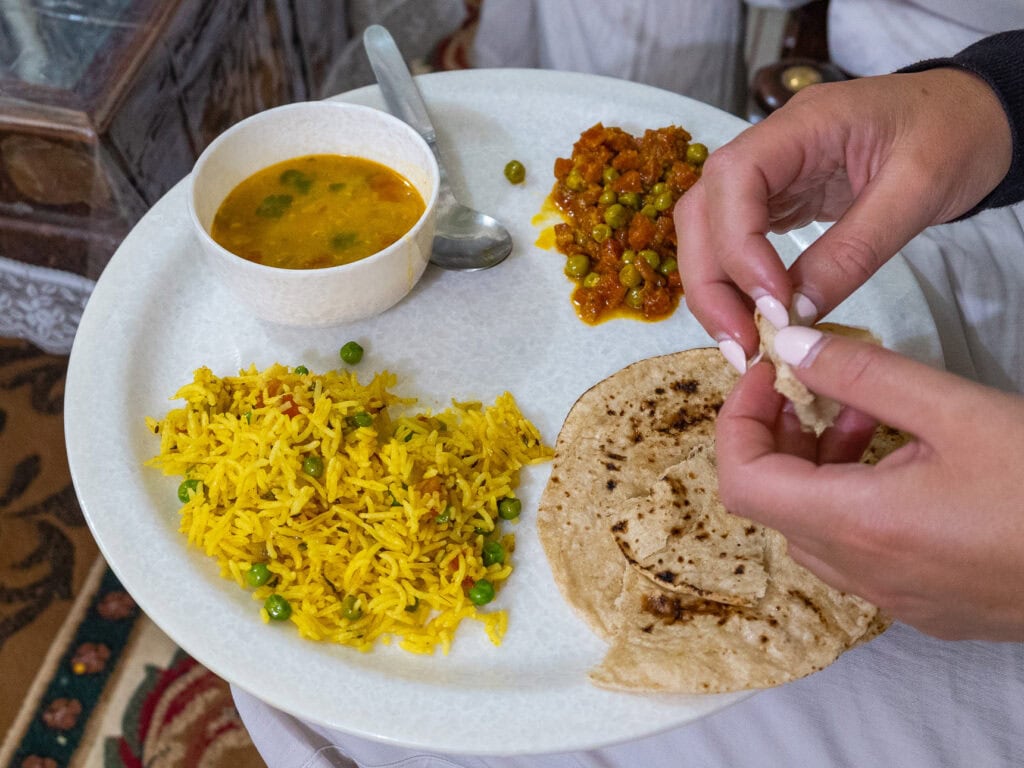 Plate of traditional Indian food with rice, curry, chapati, and lentils as a hand tears bread during a meal