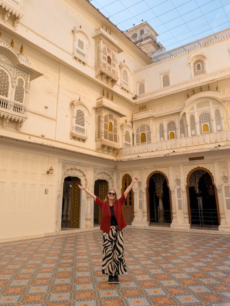 Historic courtyard in Bikaner with pale sandstone walls, arched windows, and a solo female traveller standing below