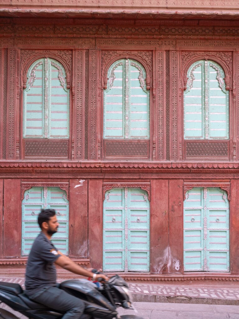 Red sandstone building in Bikaner with symmetrical windows and a man riding past in the foreground