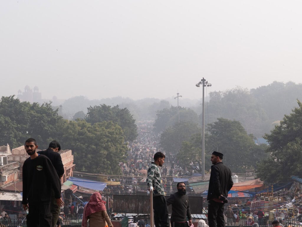 Hazy street scene in Delhi with people gathered along a busy roadside overlooking a crowded market area