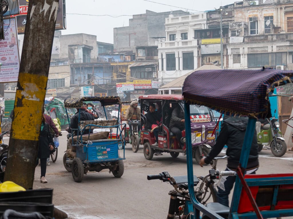 Busy street filled with tuk tuks and motorbikes moving through a hazy city, showing the fast-paced energy of urban India
