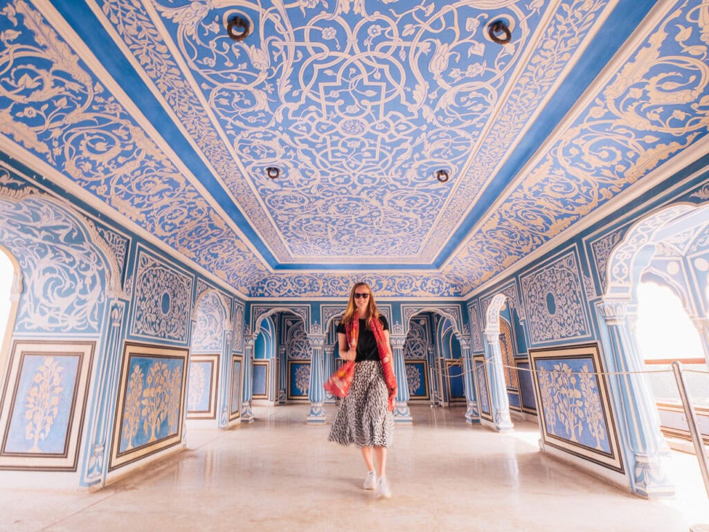 Alexx walking through a blue and white decorated hall with painted walls, arches, and patterned ceilings in Jaipur