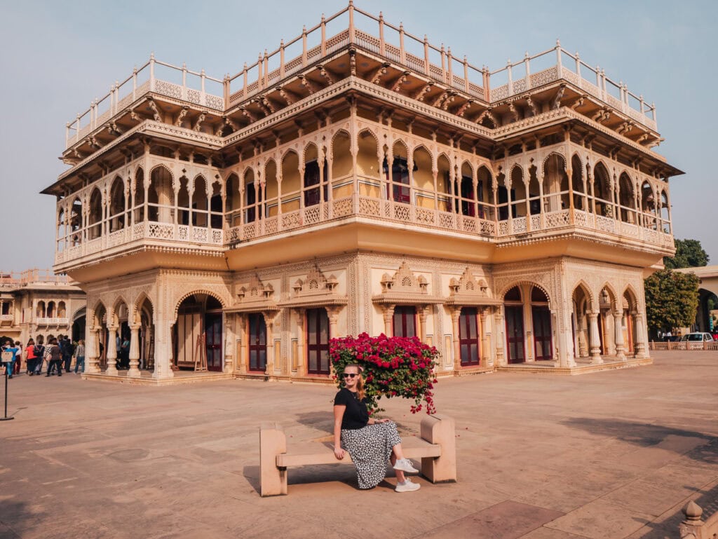 Ornate heritage building in Jaipur with detailed balconies and arches, with a solo female traveller sitting in the courtyard in front