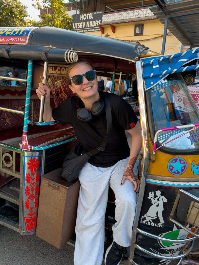 Alexx smiling from the seat of a colourful tuk tuk on a busy street, capturing a fun moment getting around
