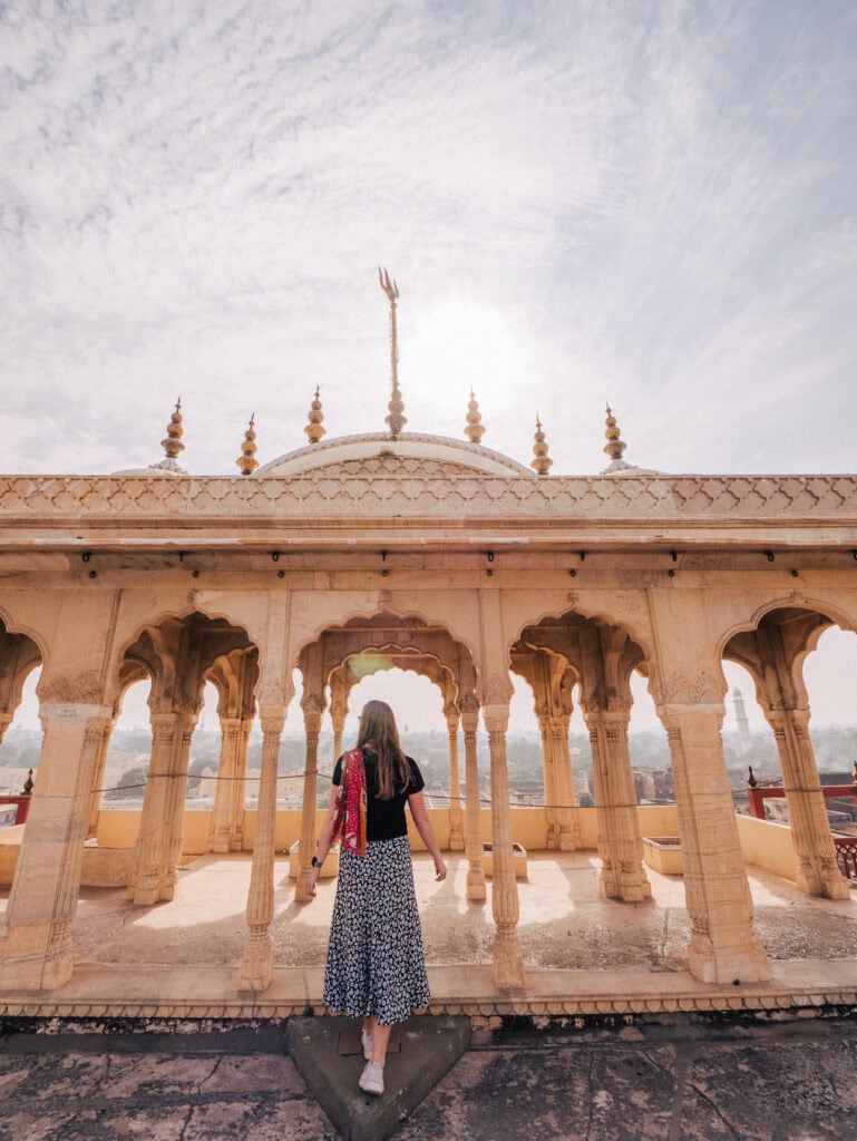 Traveller standing beneath an ornate sandstone pavilion in Jaipur with symmetrical arches and open sky above