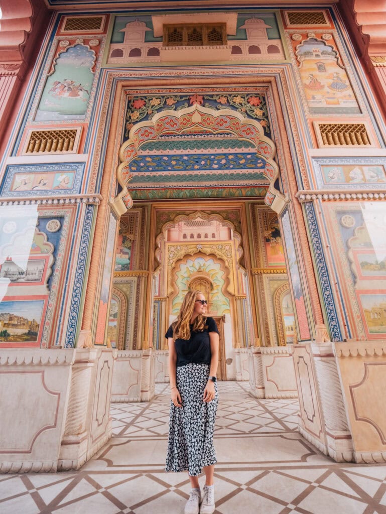 A solo female traveller walking through Patrika Gate in Jaipur with colourful painted arches and intricate symmetrical designs framing the walkway
