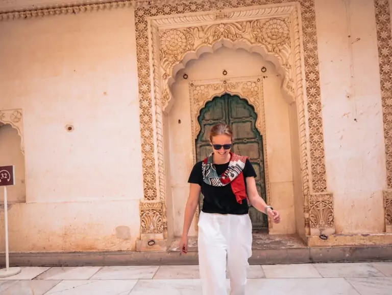 Alexx walking past an ornate arched doorway with carved stone details and a green door behind her
