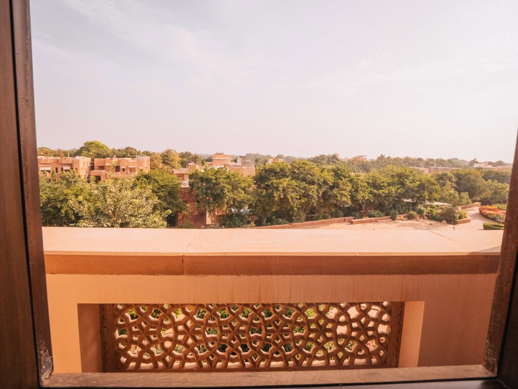 View from a balcony with a decorative railing overlooking trees and low buildings, capturing a quiet moment during a stay in India
