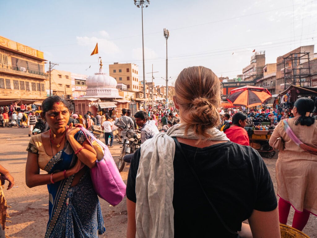 Female traveller walking through a crowded street as a local woman looks directly at her, capturing a moment of attention in a busy setting in Jodhpur, India