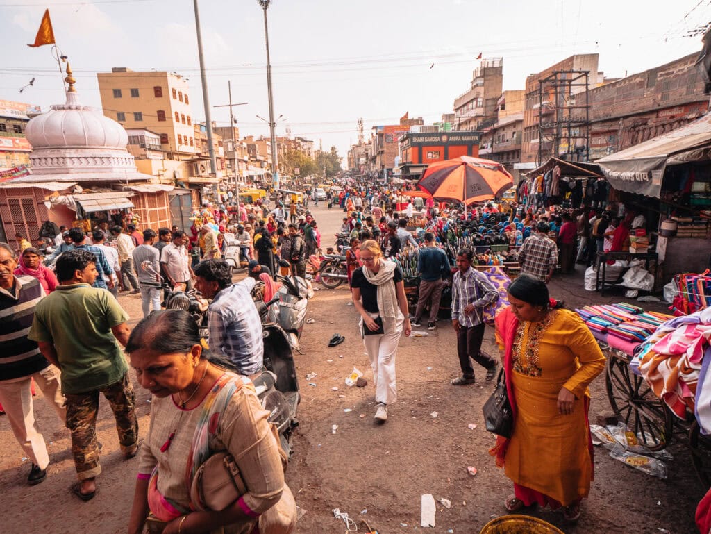 A solo female traveller in India walking through a busy street scene at Jodhpur Clock Tower Market with crowds, market stalls, and vendors lining the road.