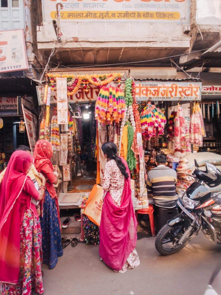 Colourful street shop in Udaipur displaying hanging fabrics and decorations as women browse outside