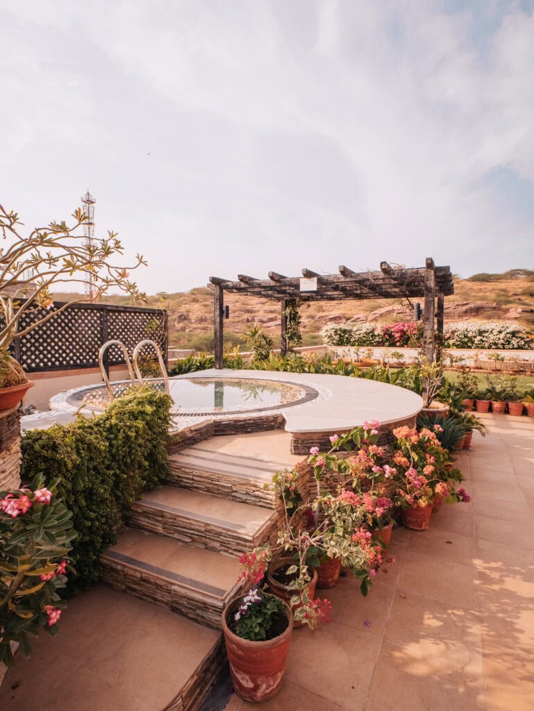Garden courtyard with stone steps leading to a small circular pool surrounded by flowers and greenery, creating a quiet retreat