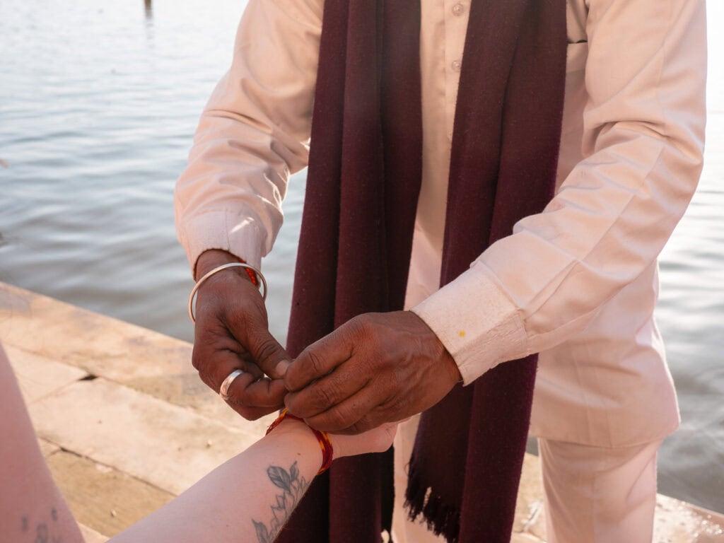 Close-up of a local priest tying a thread bracelet onto a traveller’s wrist by the water in Pushkar