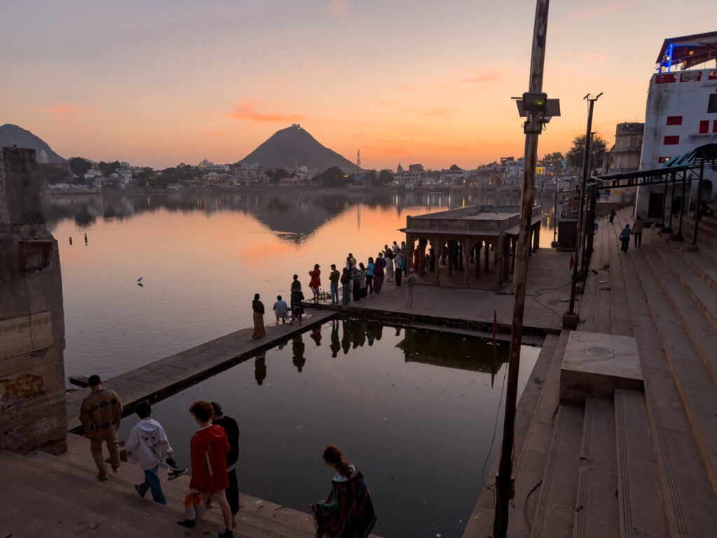 Sunset over a calm lake in Pushkar with ghats and temples in the background as people walk along the water’s edge, capturing a peaceful moment of solo female travel in India