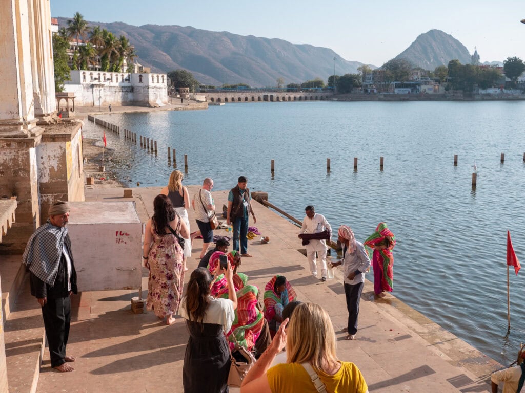 People gathered along the ghats in Pushkar by the lake as visitors watch and take photos in the warm light