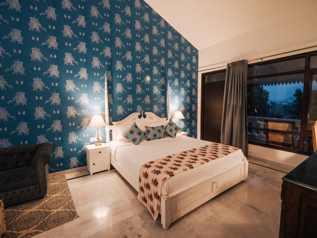 Bright bedroom at Premkunj Udaipur with patterned blue walls, a neatly made bed, and soft lighting creating a cosy atmosphere