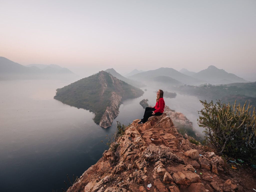 View from a nature trail near Premkunj Udaipur overlooking a calm lake and surrounding hills in soft light