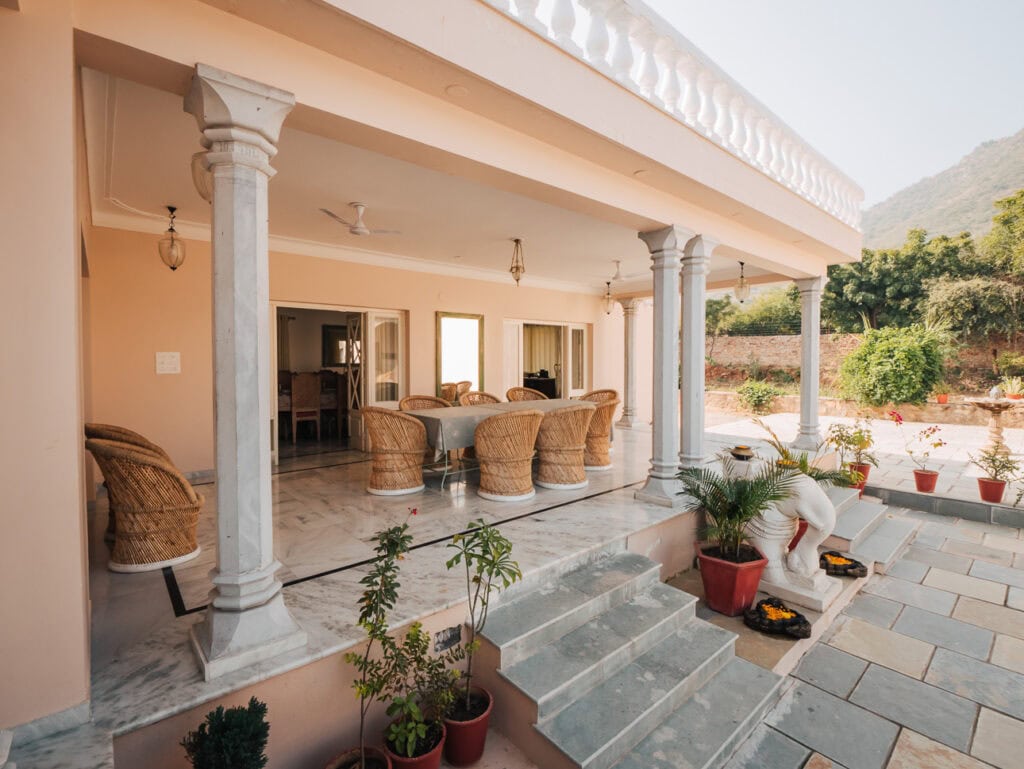 Shaded veranda at Premkunj Udaipur with wicker chairs and potted plants lining the steps, offering a relaxed place to sit
