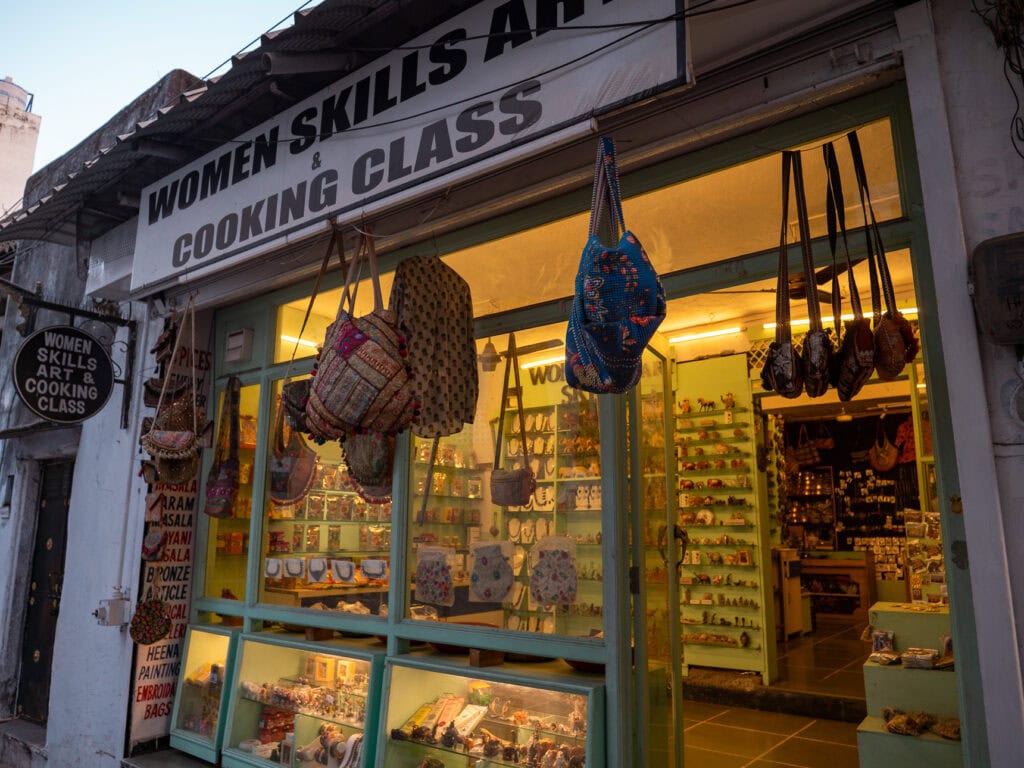Small storefront with a sign reading "Women's Skills and Cooking Class" and handmade items hanging outside, highlighting a local experience for solo female travel in India