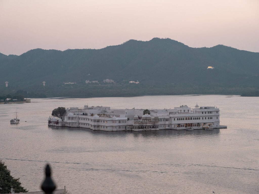 Taj Lake Palace floating on Lake Pichola in Udaipur with hazy hills in the background, seen from the waterfront