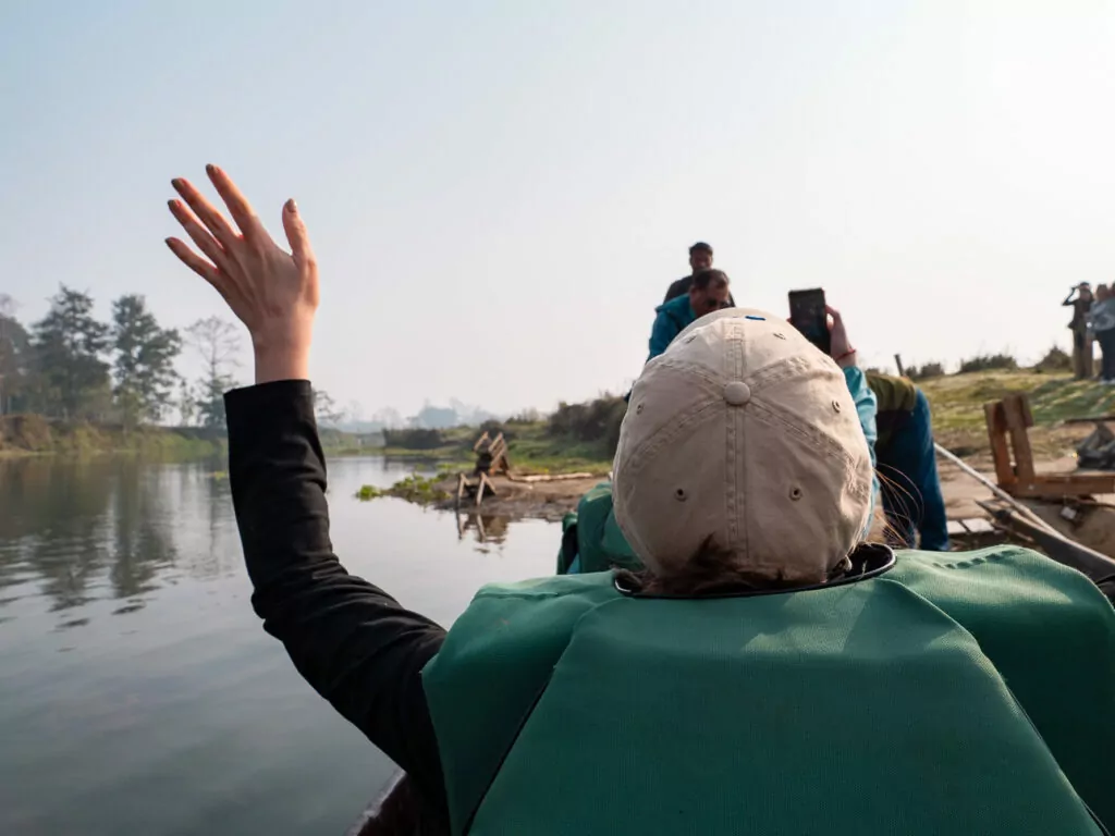 Travellers waving from a canoe on the river during a safari in Chitwan National Park