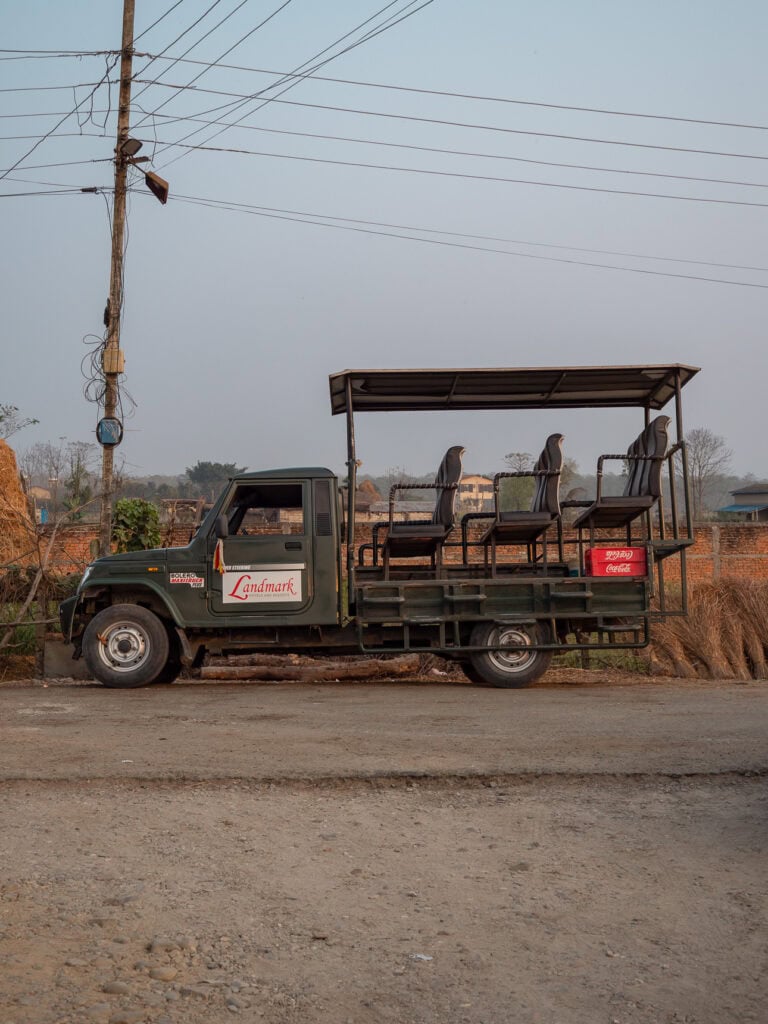 Green open-top safari vehicle parked on a dirt road in a village near Chitwan