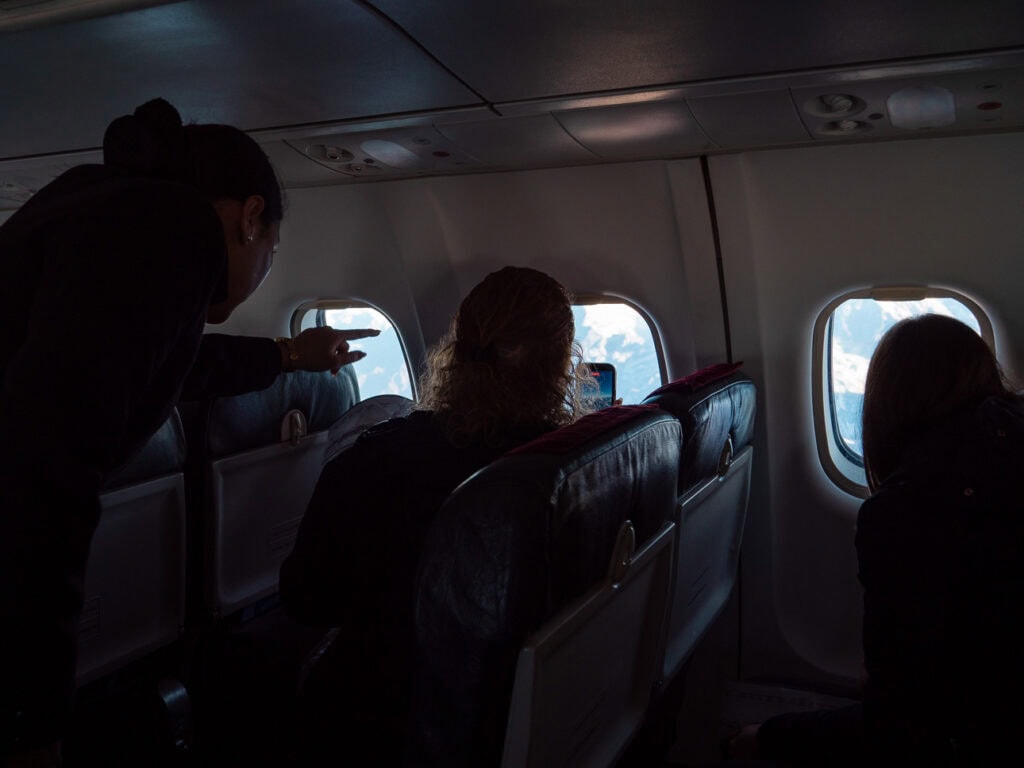 Passengers leaning towards the windows to take photos during a scenic Everest flight over the Himalayas in Nepal