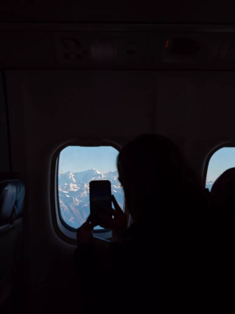 Passenger holding up a phone to photograph the Himalayas through the window of a scenic Everest flight
