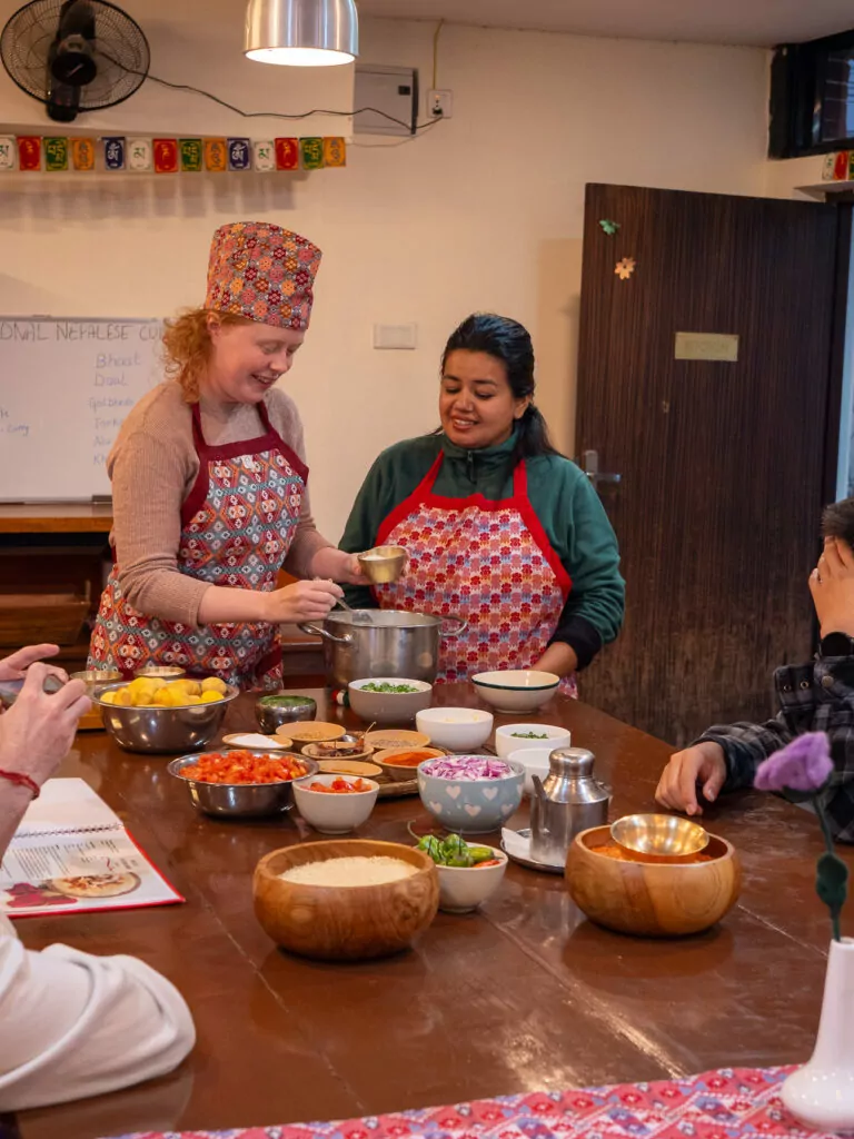 Two travellers cooking alongside a local instructor at the Sungabha Seven Sisters cooking class in Kathmandu