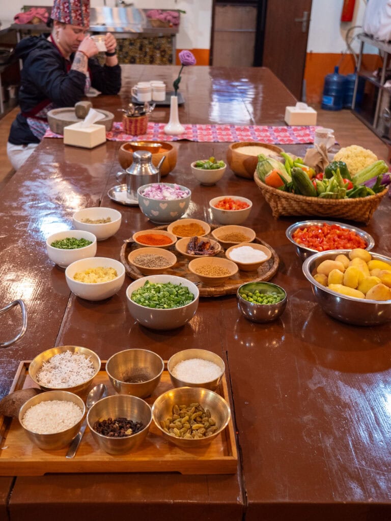 Long table filled with bowls of fresh ingredients and spices ready for a Nepali cooking class at Sungabha Seven Sisters