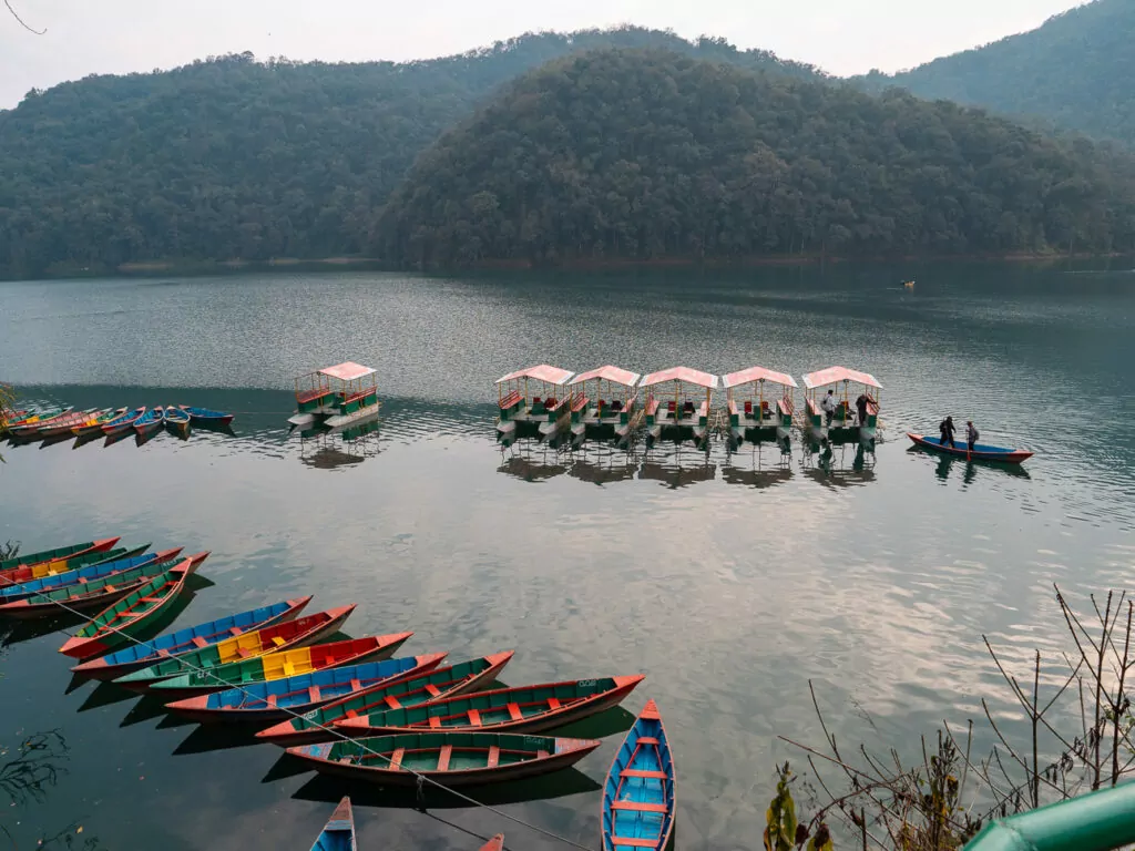 Rowing boats moored on Phewa Lake with mountains and clouds reflected in the water
