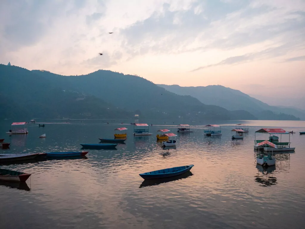 Boats on Phewa Lake in Pokhara at sunset with mountains silhouetted in the background