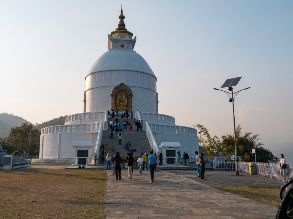The white World Peace Pagoda in Pokhara with visitors walking towards the entrance