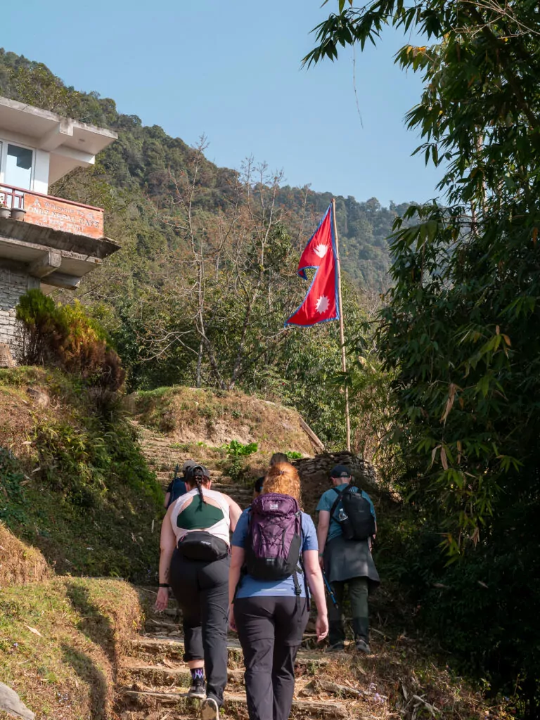 Group of trekkers with backpacks setting off on the Australian Camp trek with a Nepali flag in the background