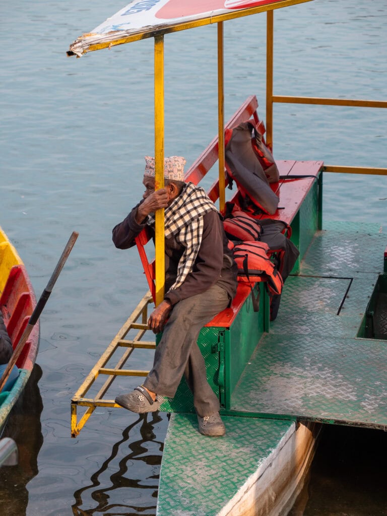 Local man sitting on a colourful boat at the shore of Lake Phewa in Pokhara
