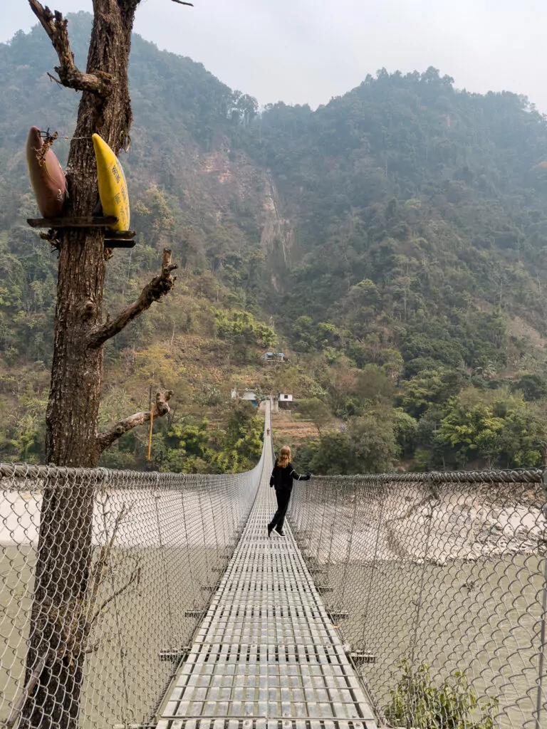 Person crossing a narrow suspension bridge over a river gorge in Nepal