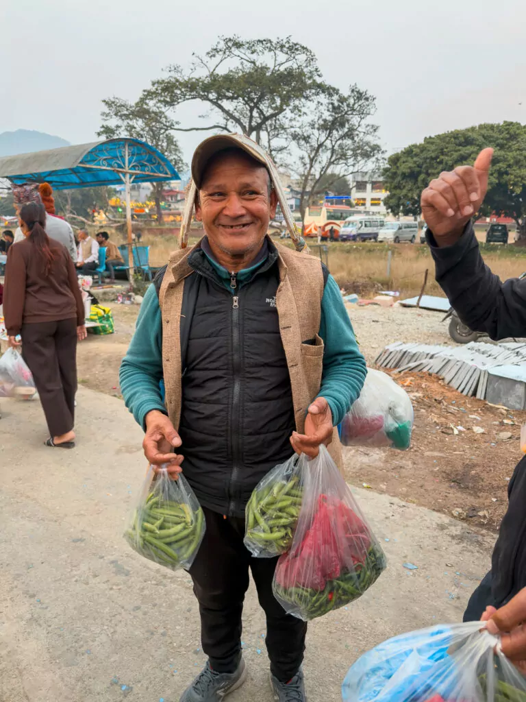 Smiling local vendor carrying bags of fresh peas on a street in Pokhara