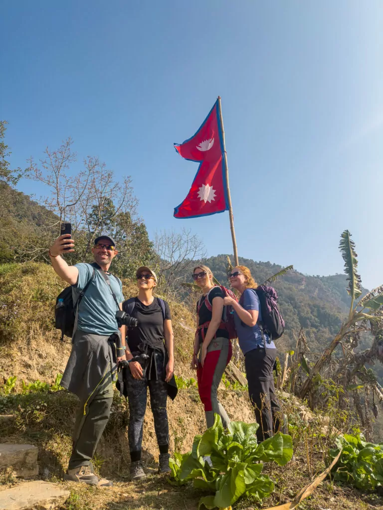 Trekkers posing for a group photo beside a Nepali flag on the Australian Camp trek during the One Life Adventures Nepal Snapshot tour