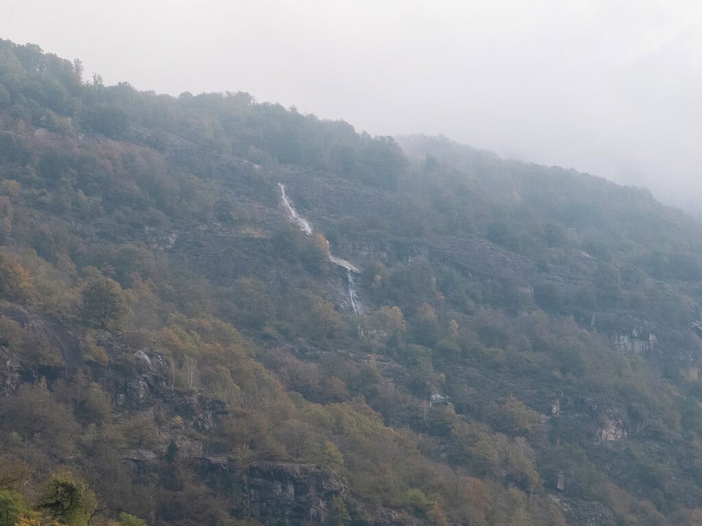 A thin waterfall cascading down a misty Leventina hillside